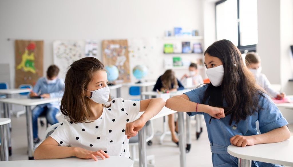 Children with face mask back at school after covid-19 quarantine and lockdown, greeting.